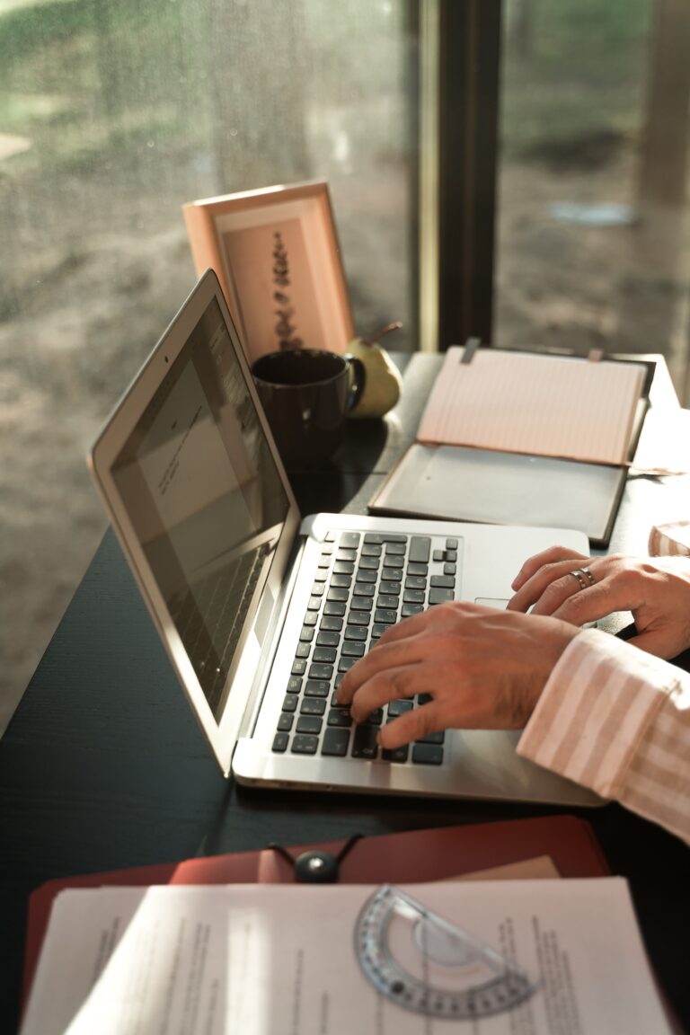 Manos tecleando en portátil con cuaderno y café, trabajo freelance de soysilviacrea desarrolladora web WordPress en Sevilla.
